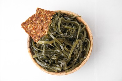 Photo of Tasty seaweed salad and crispbreads in bowl on white tiled table, top view
