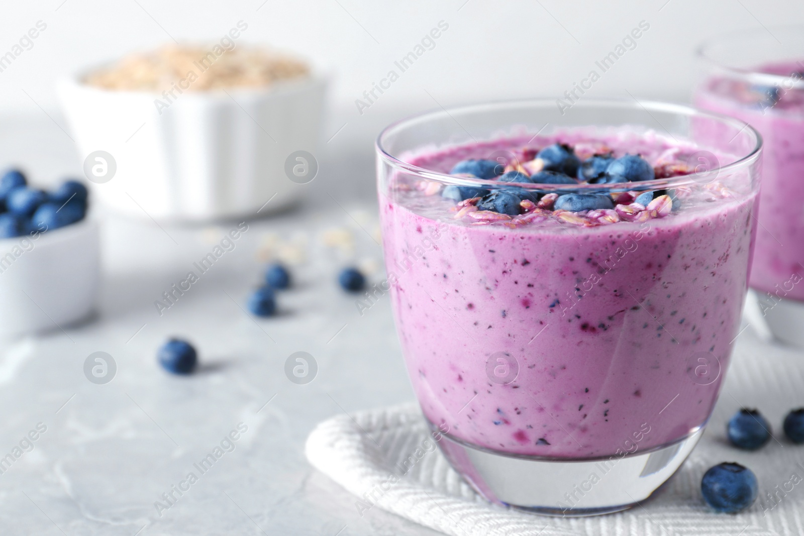 Photo of Glass of tasty blueberry smoothie with muesli on grey table. Space for text