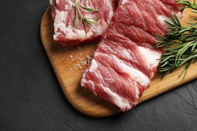 Photo of Raw ribs with rosemary and salt on black table, above view