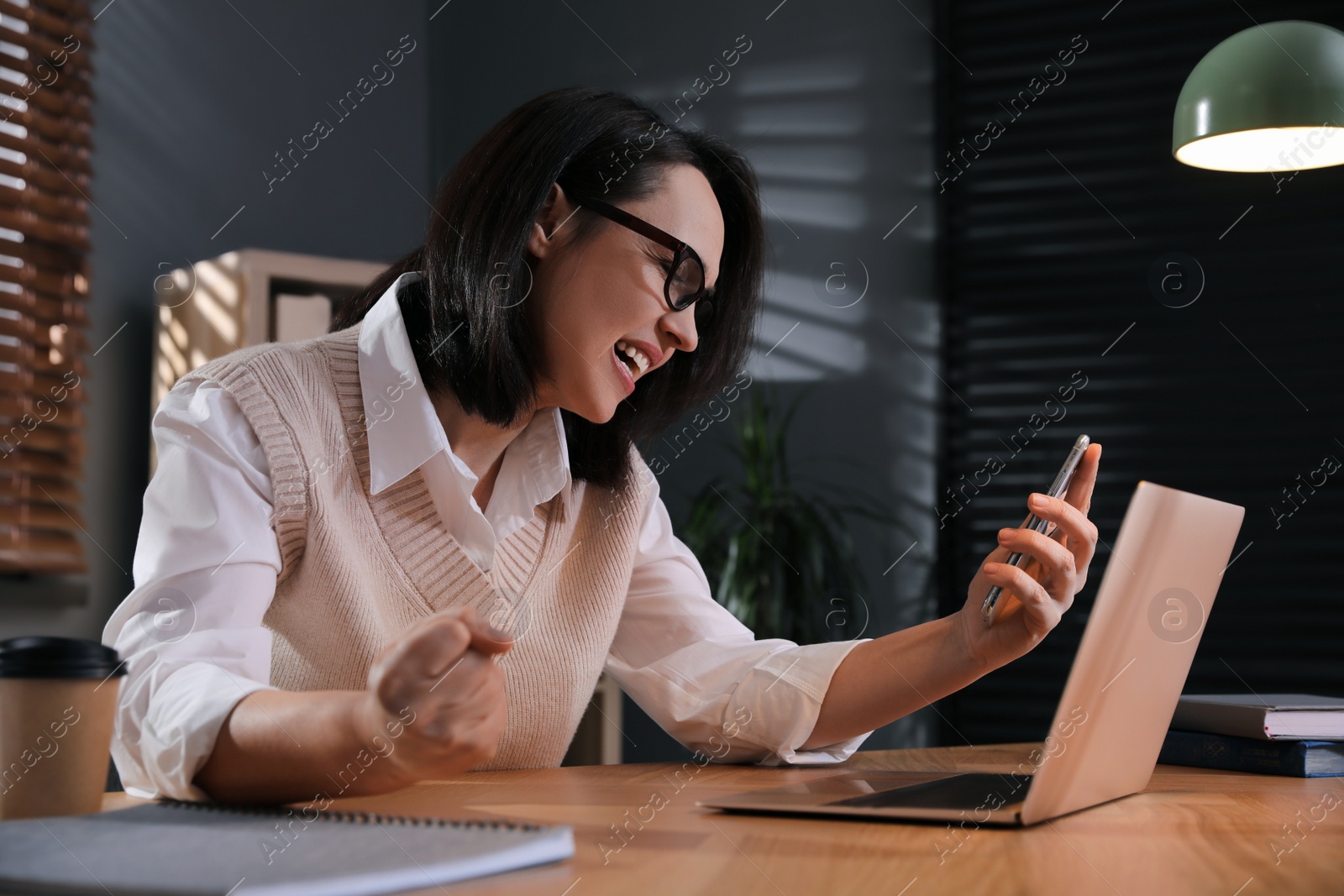 Photo of Emotional businesswoman with smartphone near laptop in office. Online hate concept