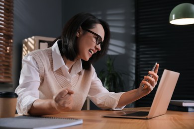 Photo of Emotional businesswoman with smartphone near laptop in office. Online hate concept