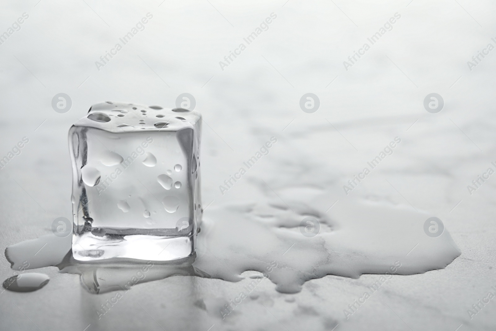 Photo of Wet ice cube on white table, closeup. Space for text