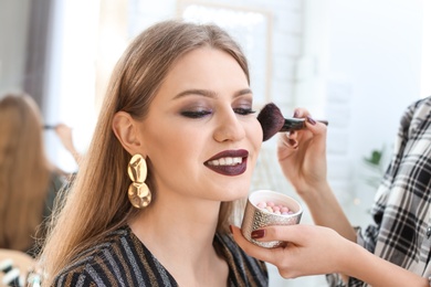 Photo of Professional makeup artist working with beautiful young woman in studio