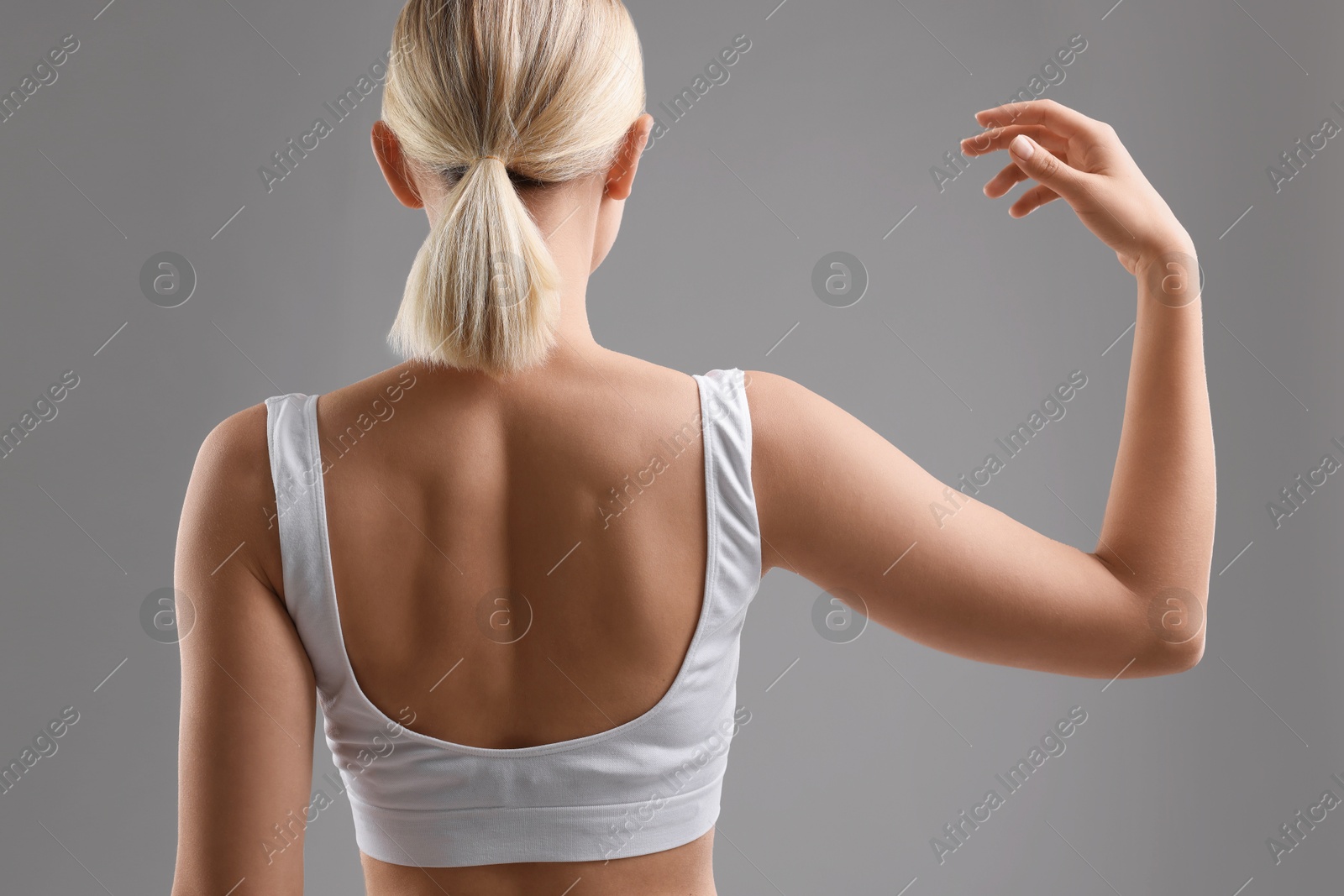 Photo of Woman showing her sporty body on grey background, back view