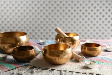 Photo of Tibetan singing bowls with mallets, candles and colorful fabric on white table