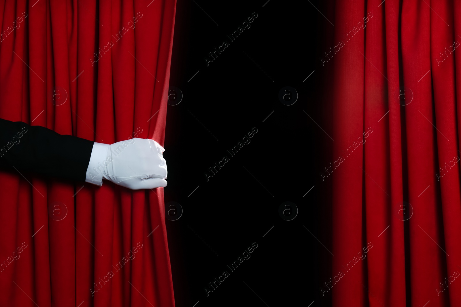 Photo of Person opening red front curtains on black background, closeup