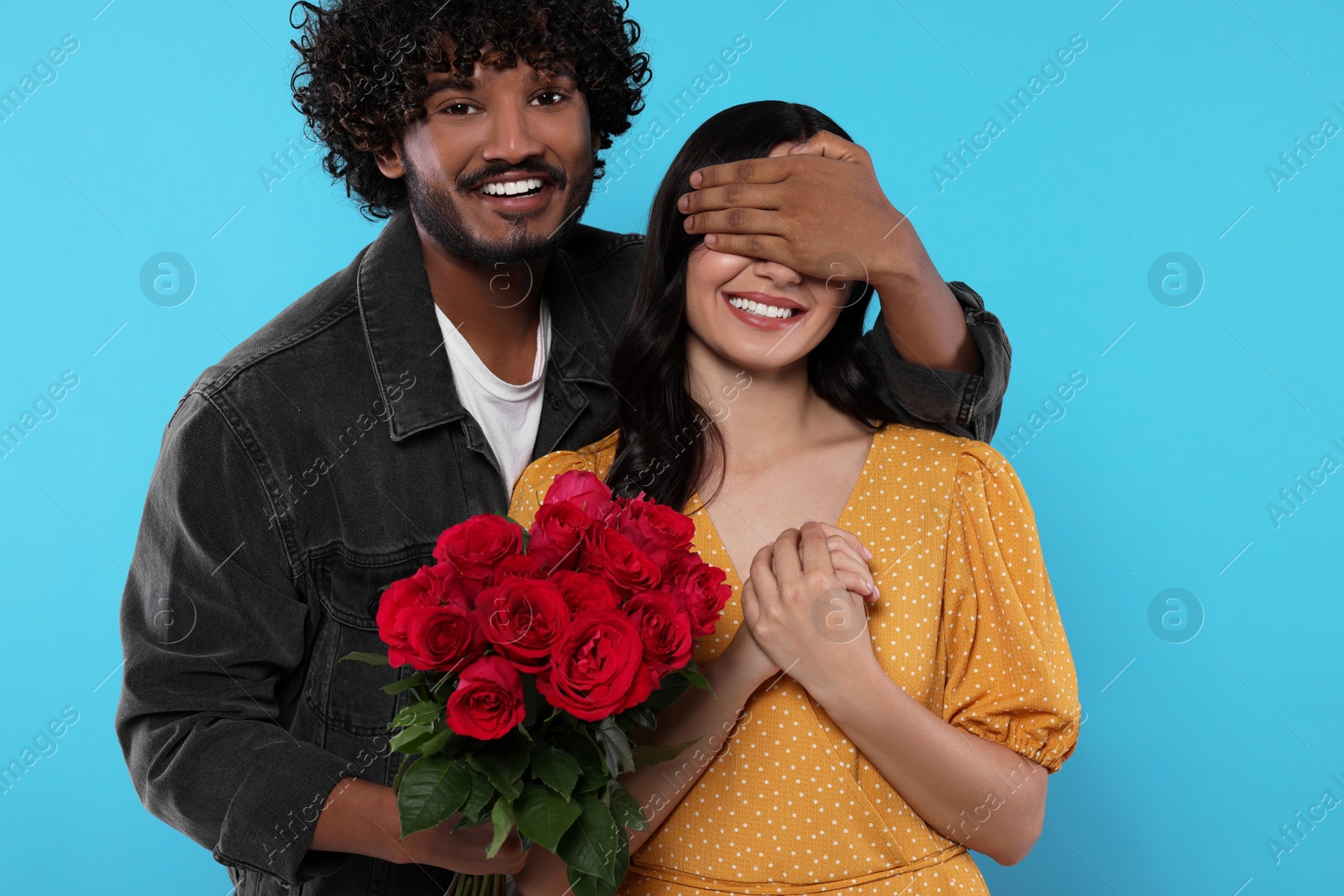 Photo of International dating. Handsome man presenting roses to his beloved woman on light blue background