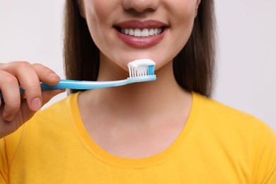 Photo of Woman holding plastic toothbrush with toothpaste on white background, closeup