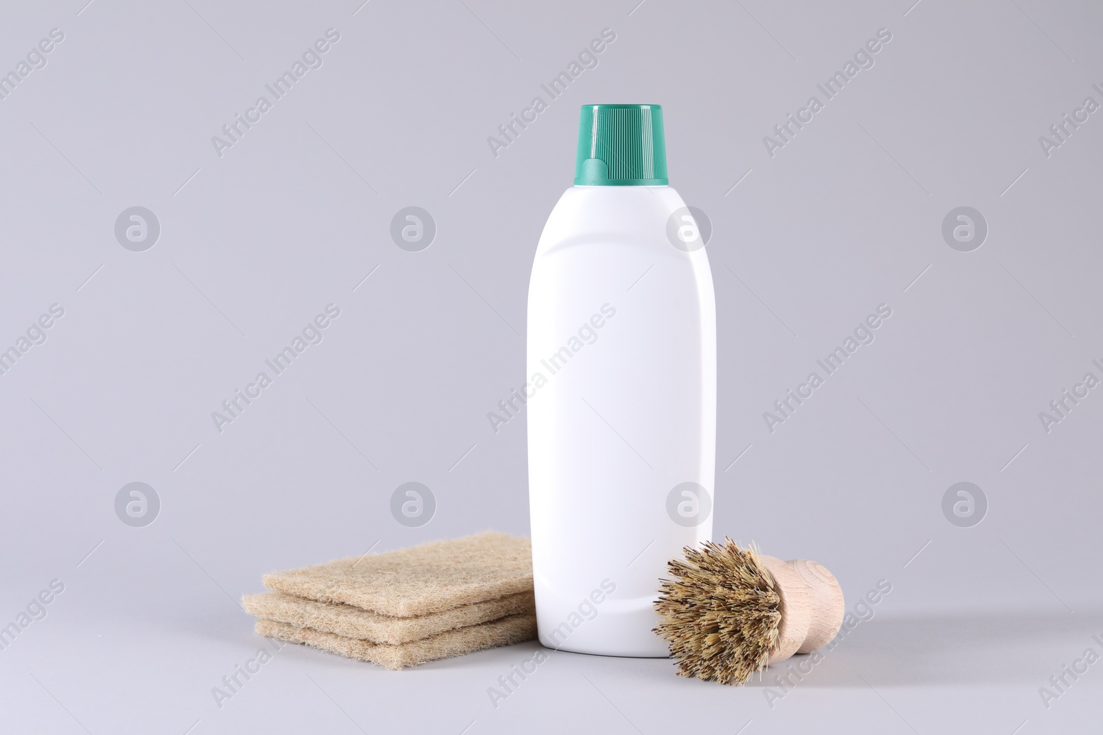 Photo of Bottle of cleaning product, brush and sponges on light background