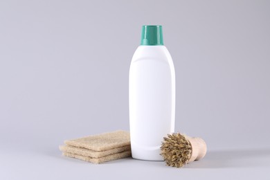 Bottle of cleaning product, brush and sponges on light background