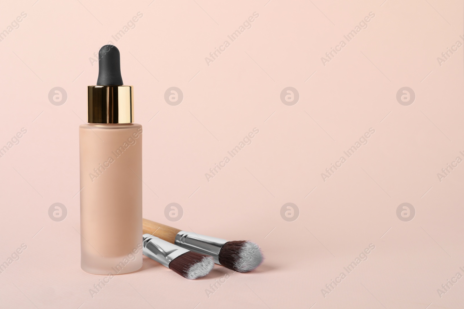 Photo of Bottle of skin foundation and brushes on beige background, space for text. Makeup product