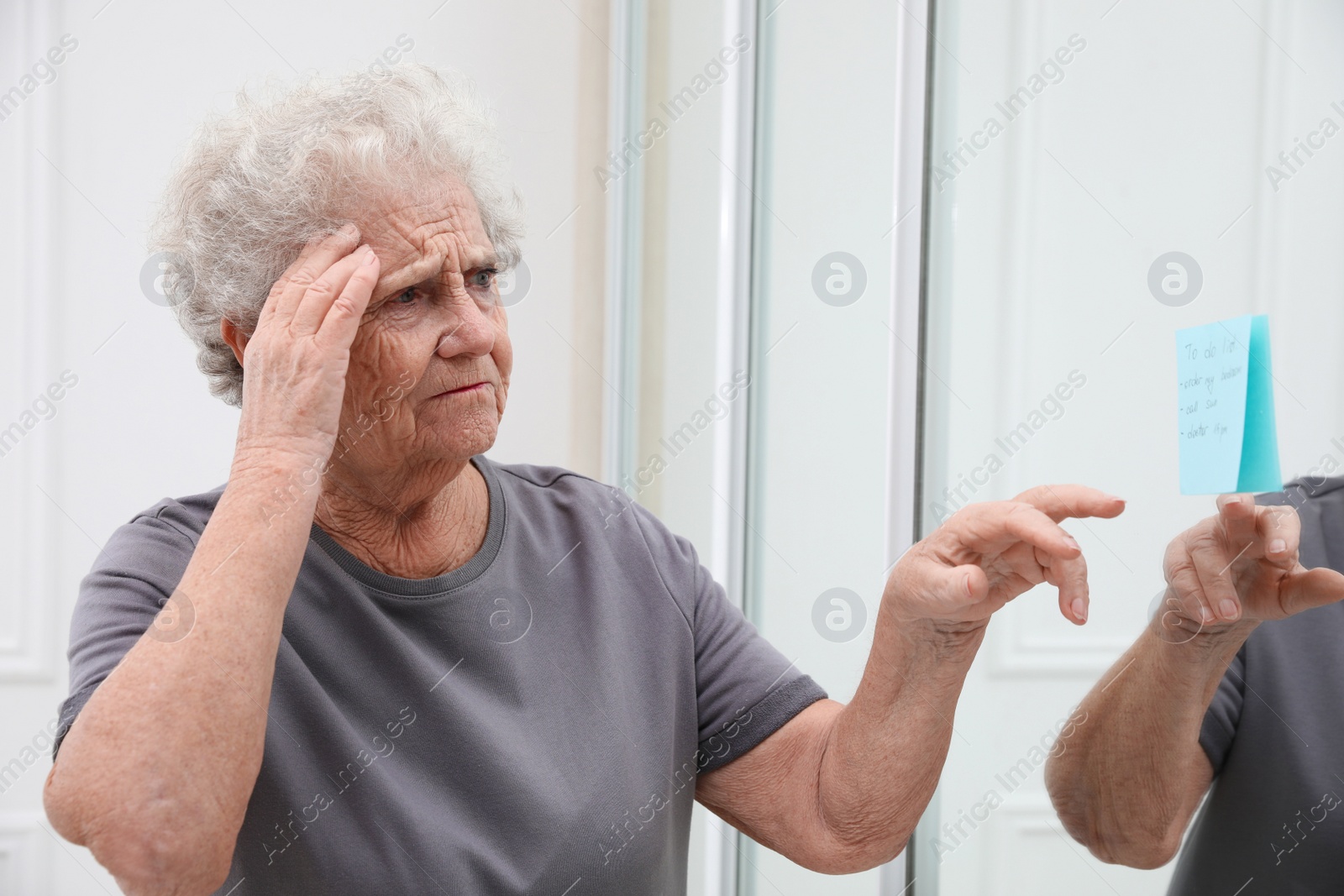 Photo of Senior woman looking at reminder note indoors. Age-related memory impairment