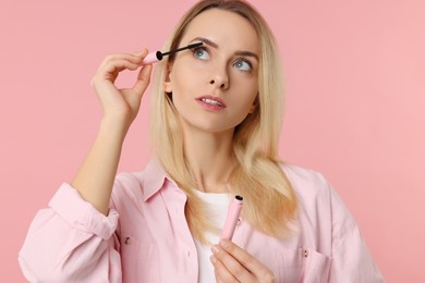 Photo of Beautiful woman applying mascara on pink background