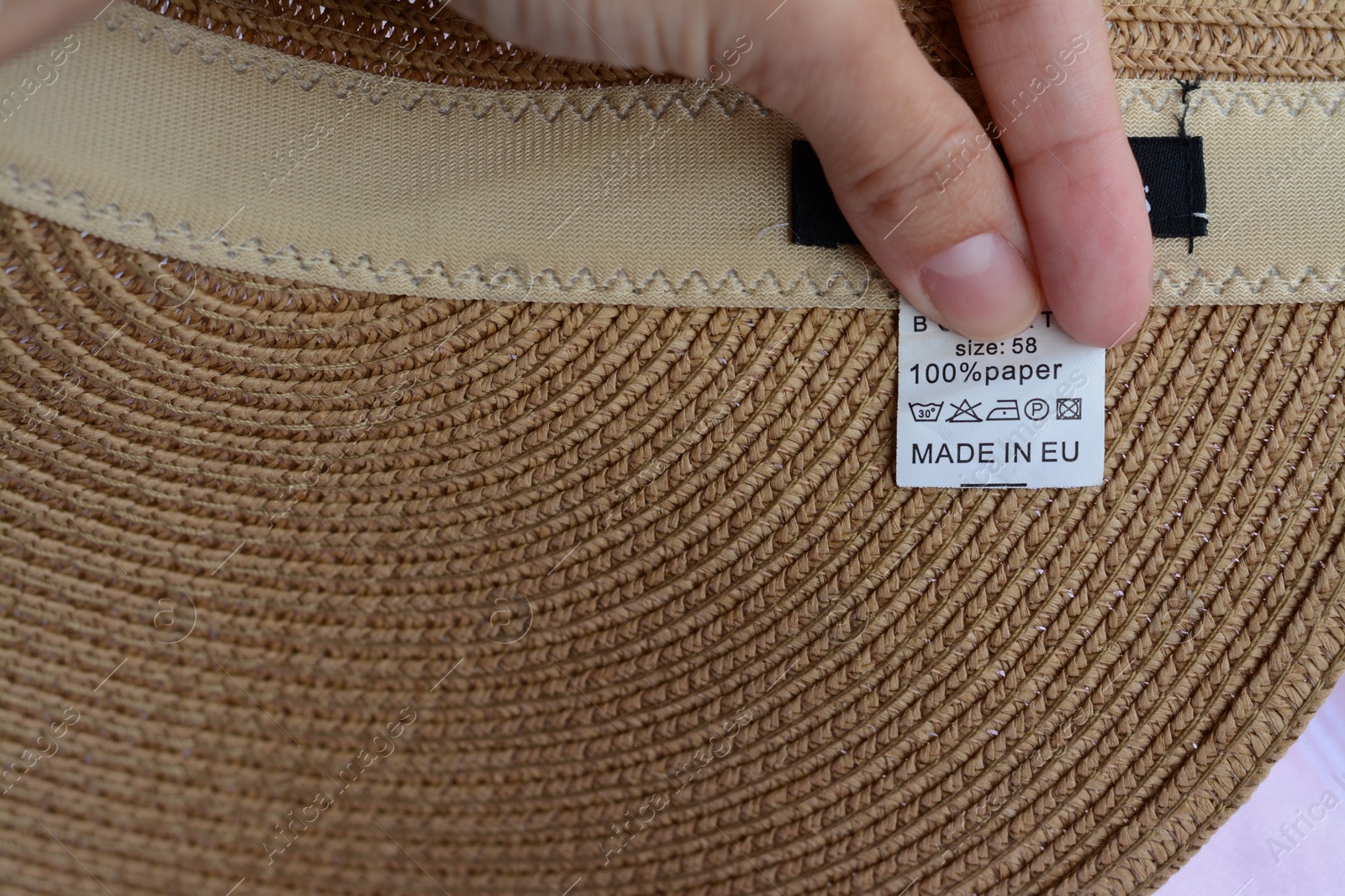 Photo of Woman holding white clothing label on hat, closeup. Space for text