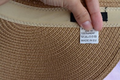 Photo of Woman holding white clothing label on hat, closeup. Space for text