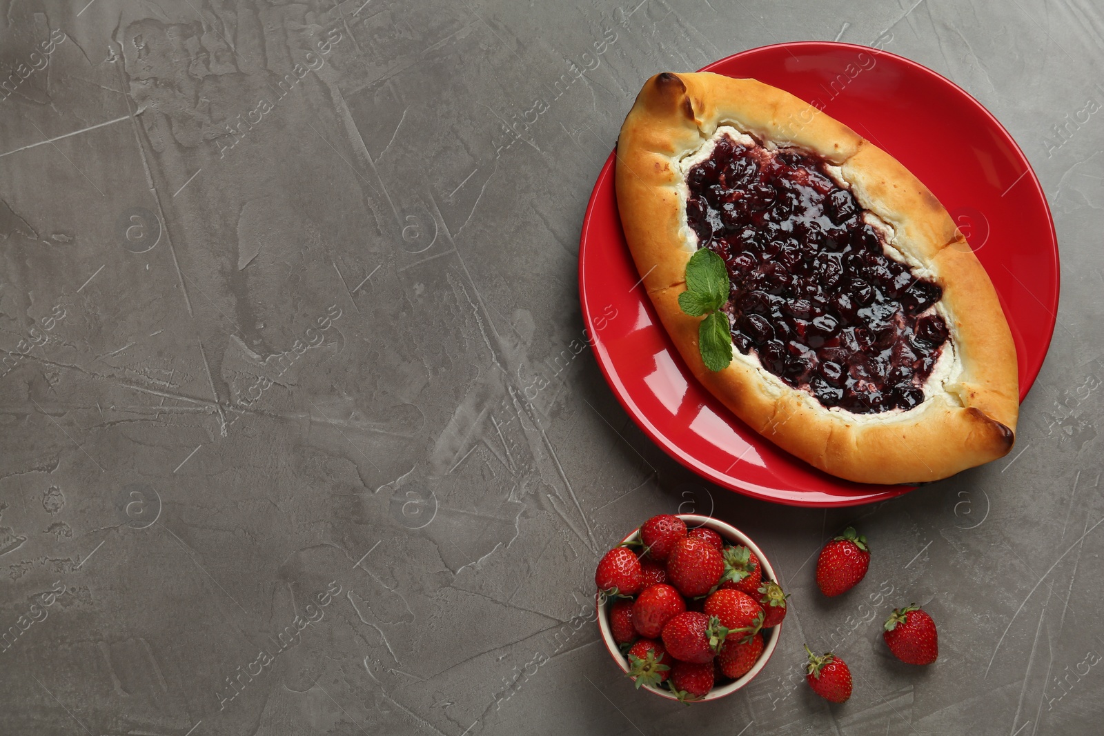 Photo of Delicious sweet cottage cheese pastry with cherry jam and fresh strawberries on grey table, flat lay. Space for text