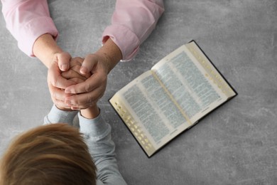 Photo of Boy and his godparent praying together at grey table, closeup