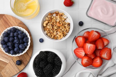 Tasty oatmeal, fresh berries, yogurt and honey on white tiled table, flat lay. Healthy breakfast