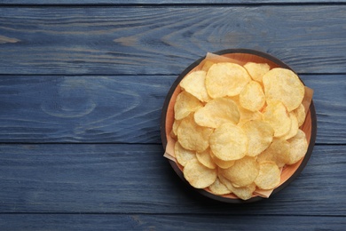 Bowl of potato chips on wooden table, top view. Space for text