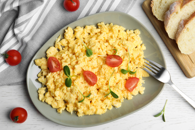 Photo of Tasty scrambled eggs served on white wooden table, flat lay