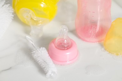 Wet baby bottles and nipple after sterilization near brush on white table, above view