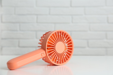 Photo of Portable fan on table near white brick wall. Summer heat