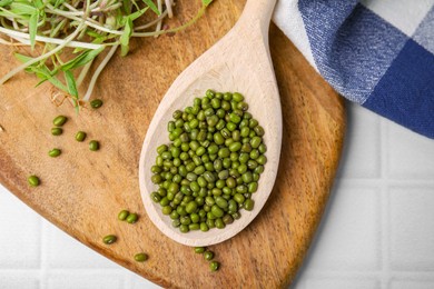 Photo of Wooden spoon with mung beans and board on white tiled table, flat lay