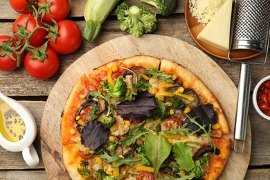 Delicious vegetarian pizza and ingredients on wooden table, flat lay