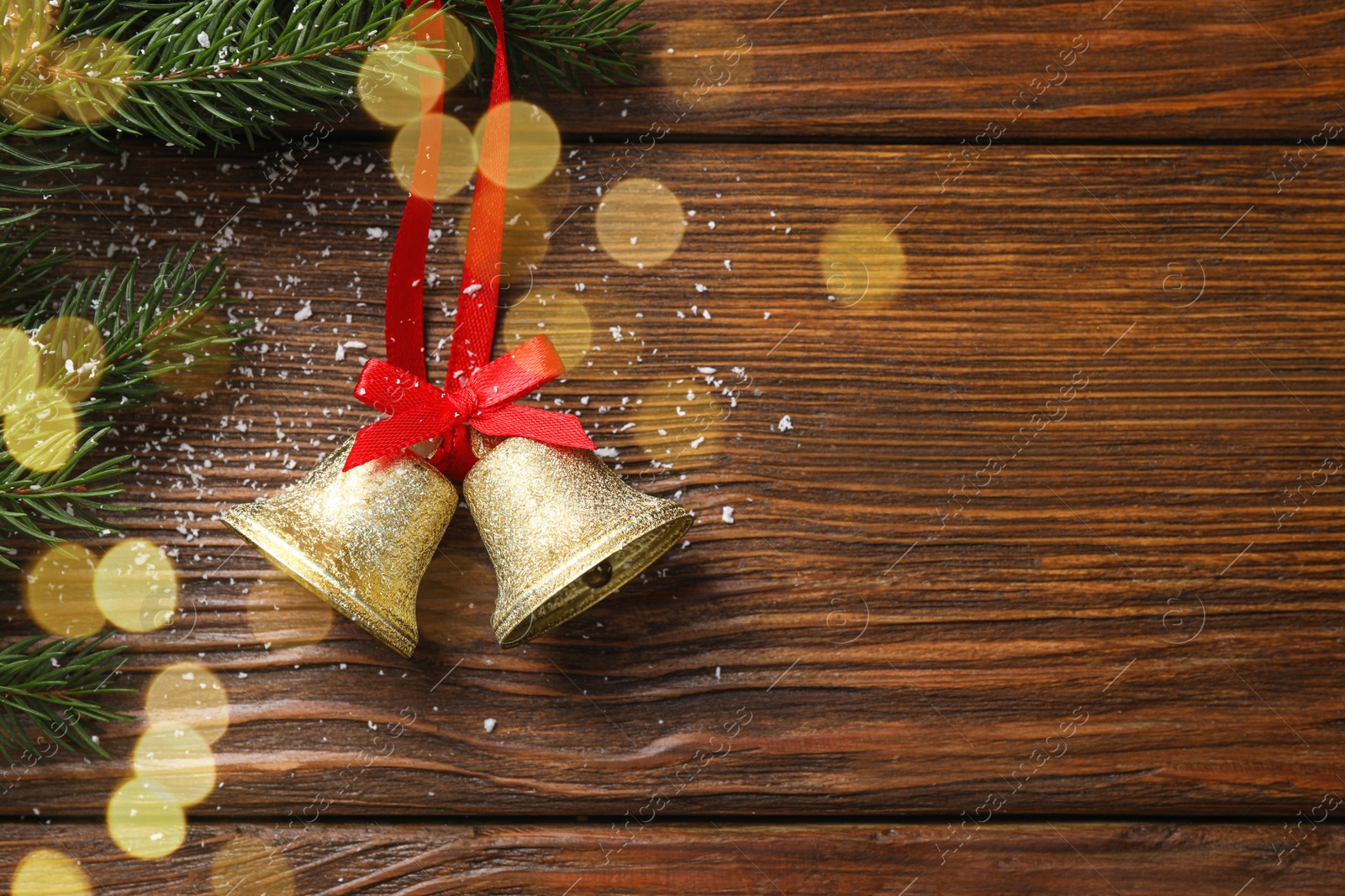 Photo of Christmas bells and fir tree branches on wooden table, flat lay. Space for text