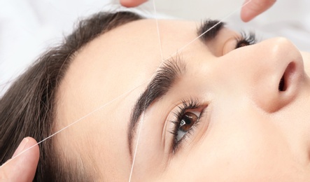 Photo of Young woman having professional eyebrow correction procedure in beauty salon, closeup