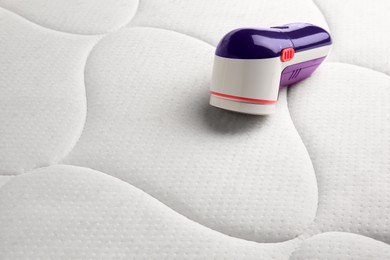 Photo of Modern fabric shaver on mattress with lint. Space for text