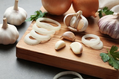 Photo of Wooden board with garlic and onion rings on table, closeup