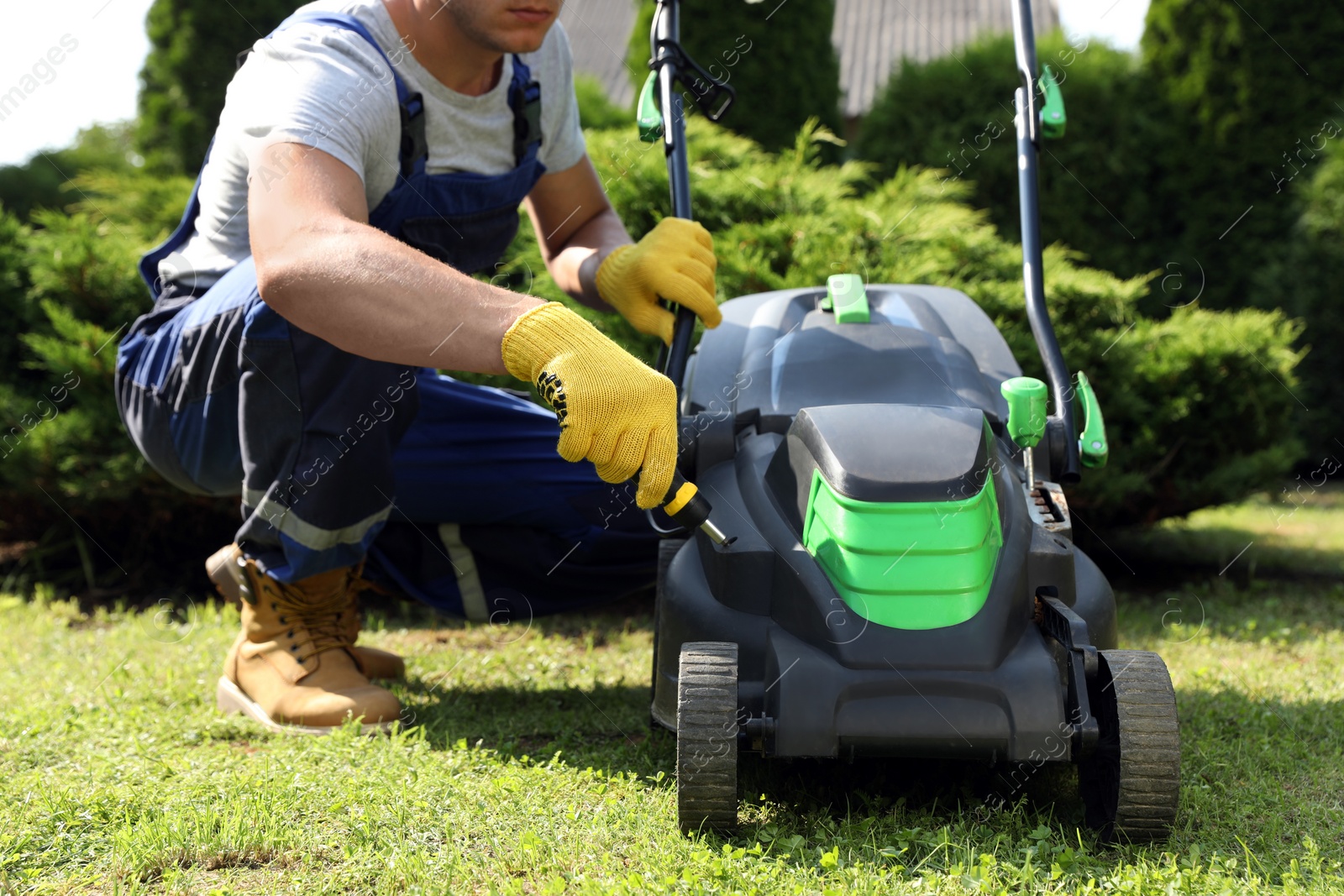 Photo of Young man with screwdriver fixing lawn mower in garden, closeup