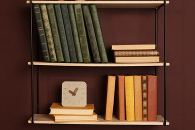 Shelves with different books and clock on brown wall