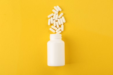 Bottle and vitamin capsules on yellow background, top view