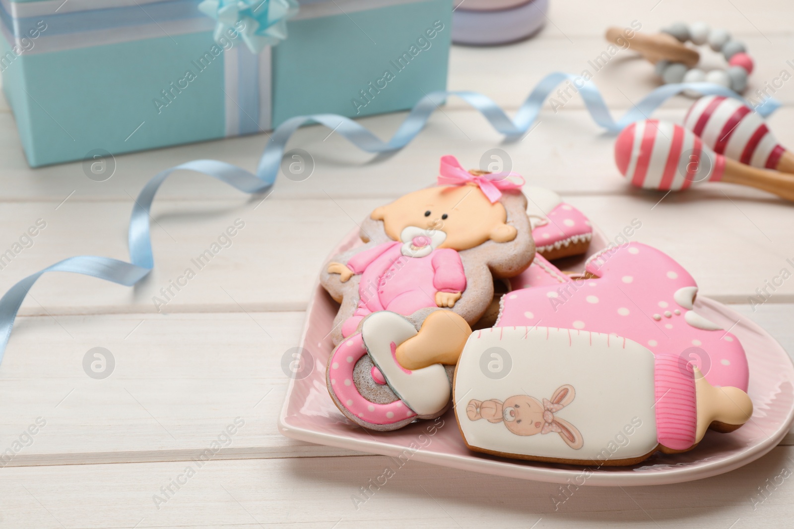 Photo of Heart shaped plate of baby shower cookies and accessories on white wooden table