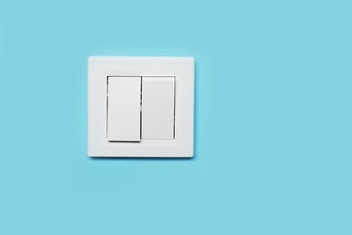 Modern plastic light switch on blue wall, space for text