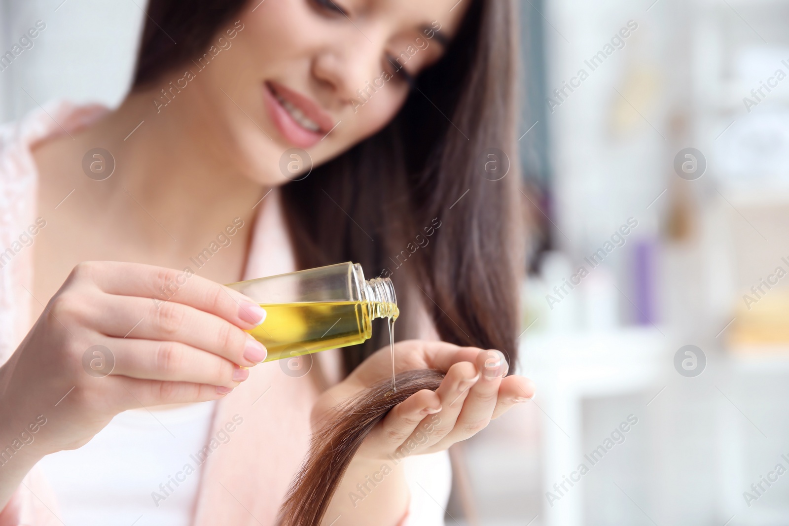 Photo of Young woman applying oil onto hair at home