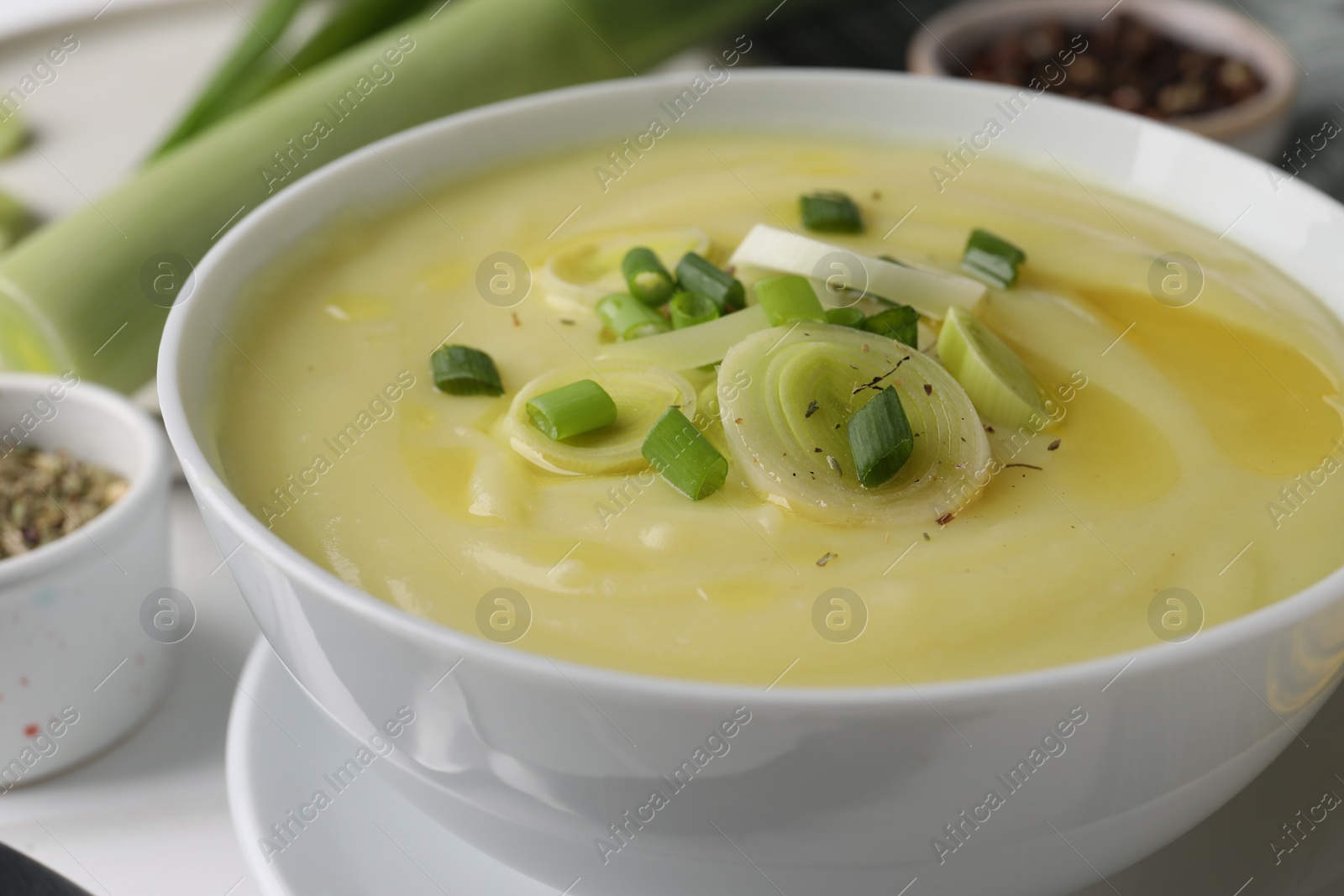 Photo of Bowl of tasty cream soup with leek on white table, closeup