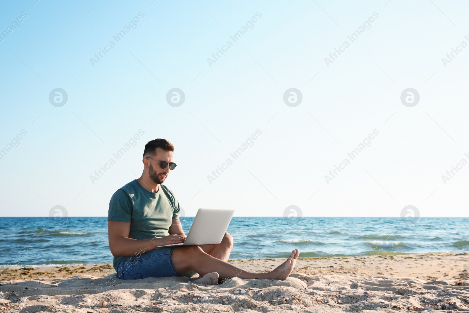 Photo of Man working with laptop on beach. Space for text