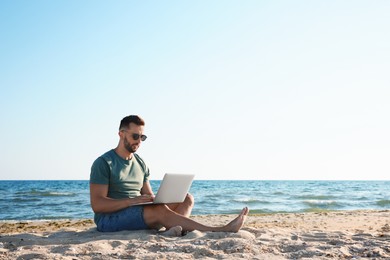 Photo of Man working with laptop on beach. Space for text