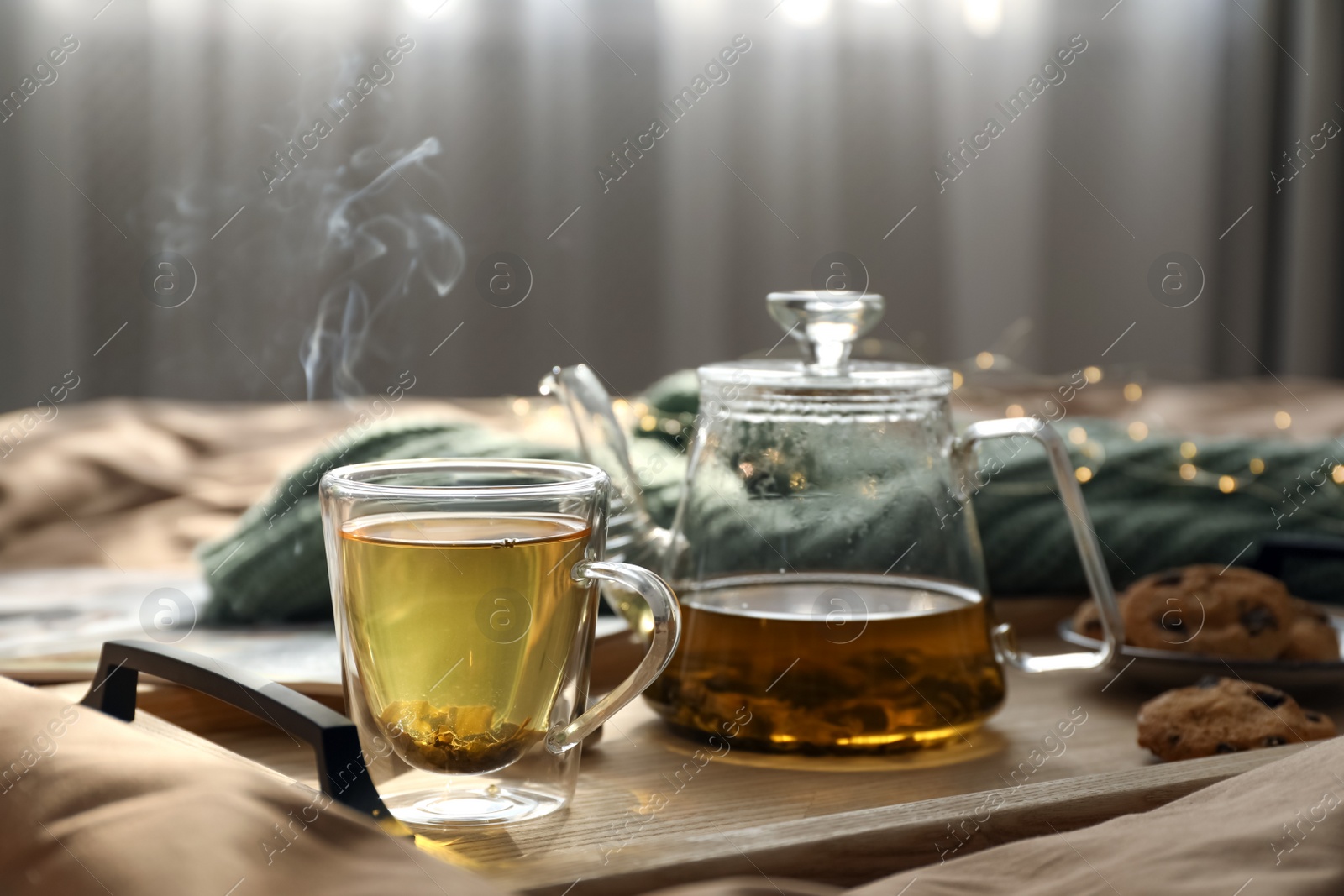 Photo of Wooden tray with freshly brewed tea and cookies on bed in room. Cozy home atmosphere