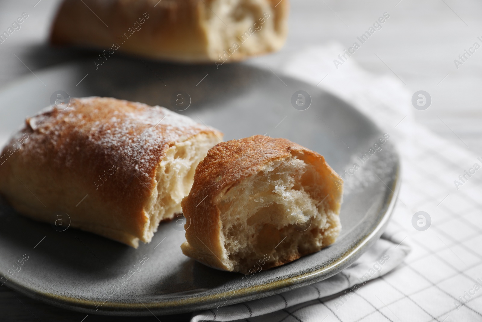 Photo of Fresh crispy ciabattas on white checkered tablecloth, closeup