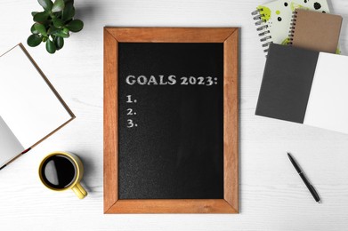 Image of Blackboard with phrase GOALS 2023 and empty checklist on white wooden background, flat lay