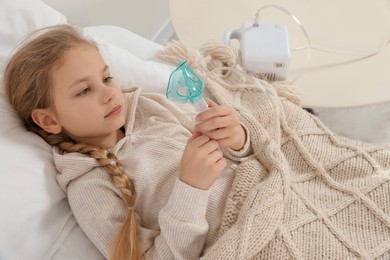 Photo of Little girl holding nebulizer for inhalation on bed at home
