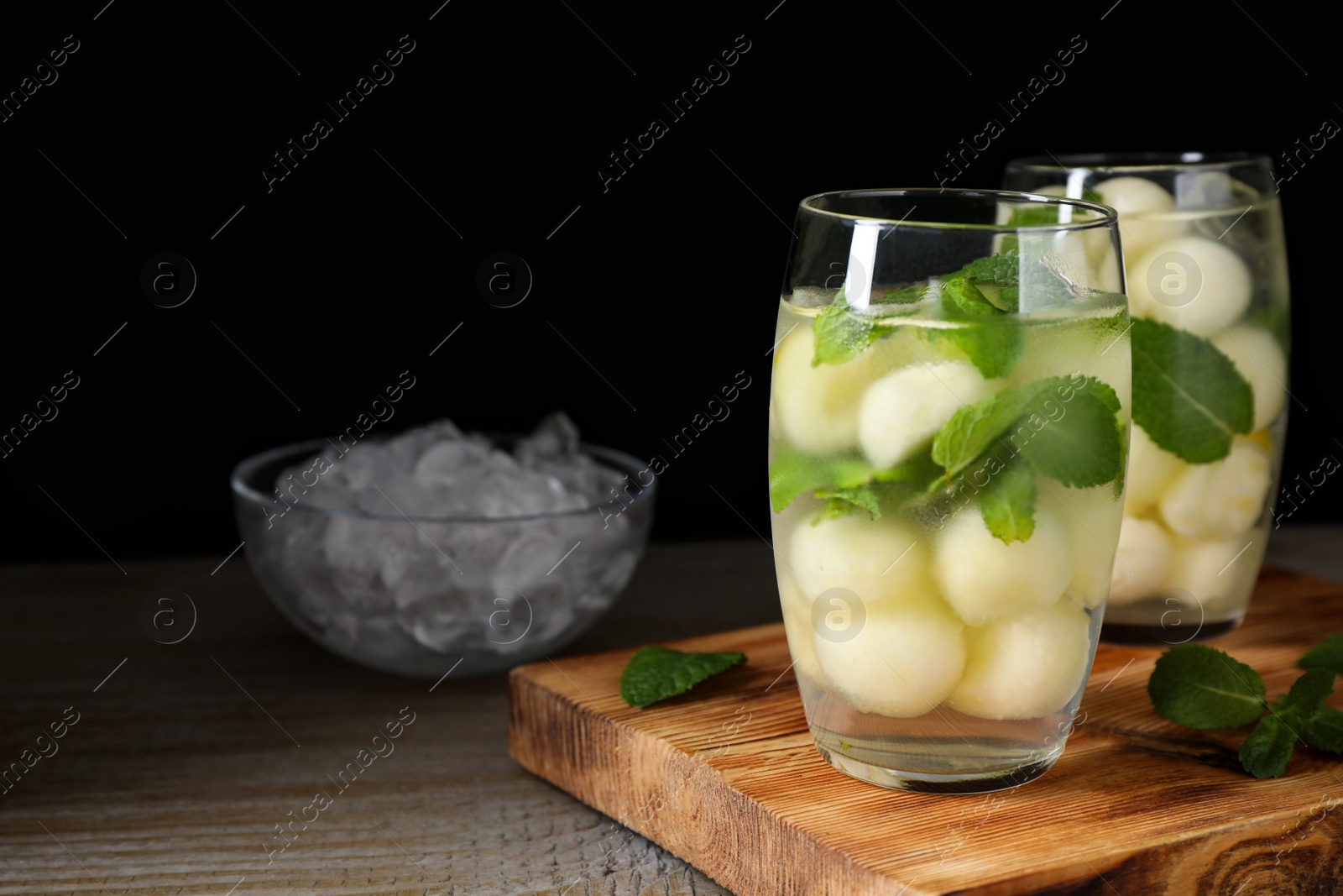 Photo of Tasty melon ball drink on wooden table against black background. Space for text