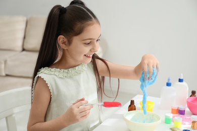 Cute little girl making DIY slime toy at table in room