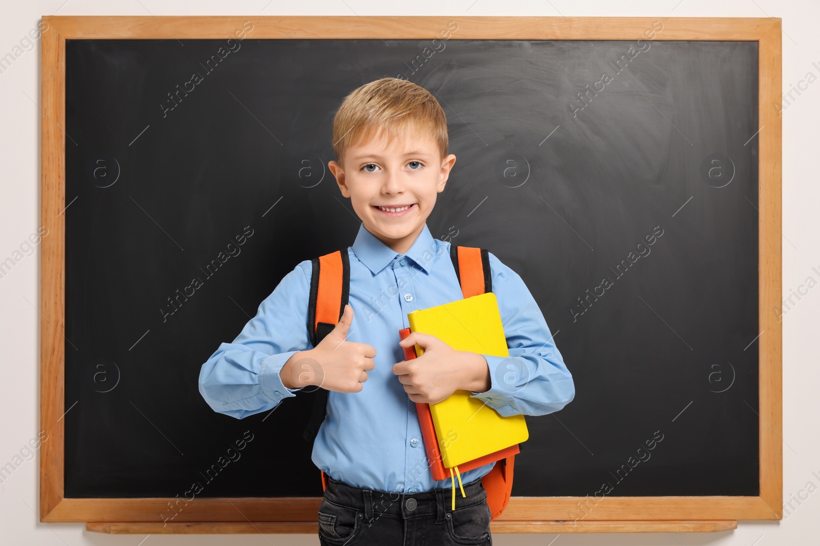Photo of Happy schoolboy with backpack and books near blackboard