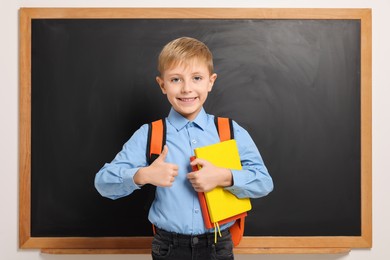 Happy schoolboy with backpack and books near blackboard