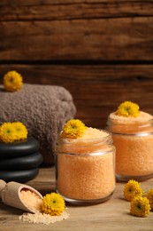 Jars with orange sea salt, spa stones, towel and beautiful flowers on wooden table